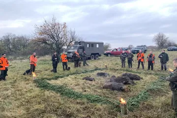 Výlož diviakov, poľovníci a vodiči psov na lúke pri terénnych autách